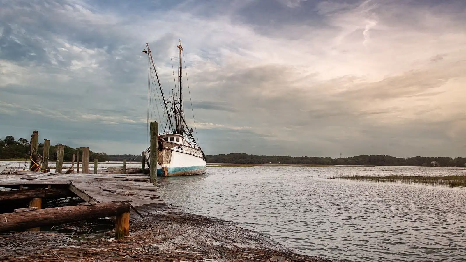 A small passenger boat tied up at a wooden dock on an overcast day