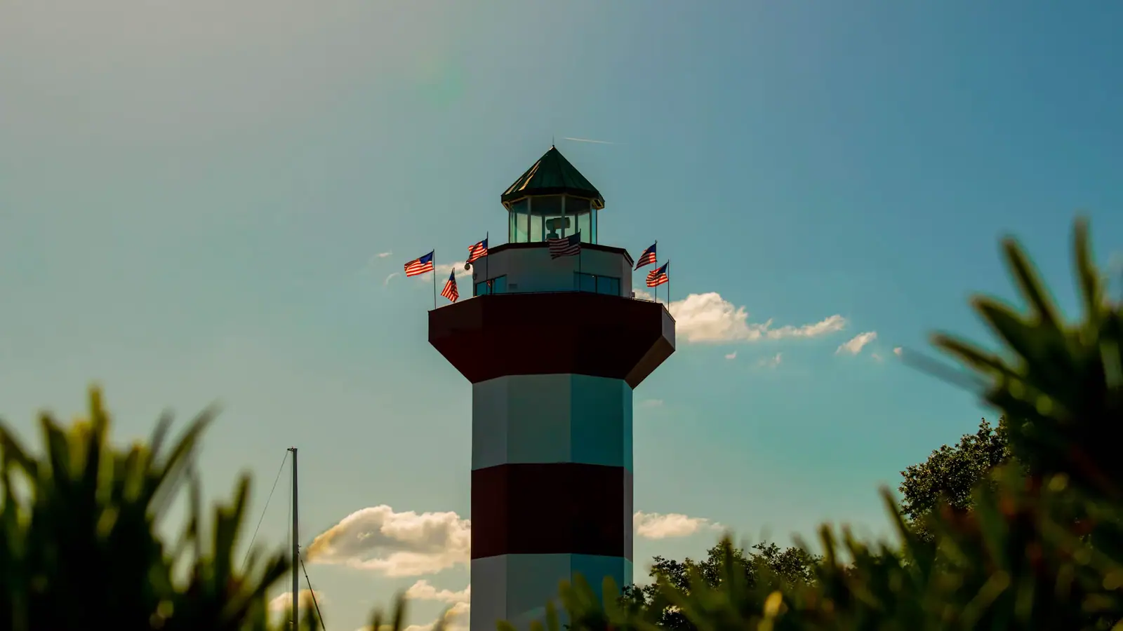 A red-and-white striped lighthouse rising above a dense treeline