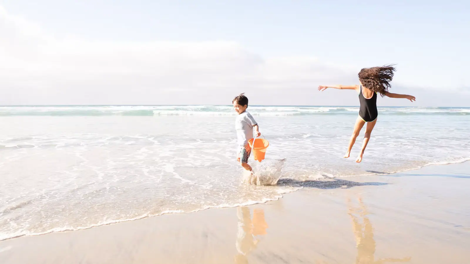 Two children running along the wet sand at the edge of the water